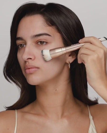 Model brengt de Changing Foundation aan met een dubbelzijdige kwast voor een natuurlijke glow en houdt vervolgens de foundationfles vast.